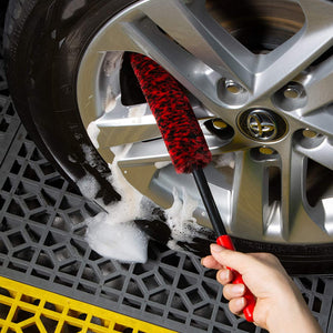 Person cleaning car wheel with a red brush on a soapy surface