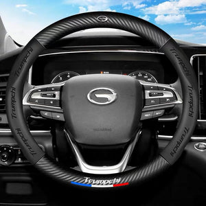Car steering wheel with carbon fiber texture and 'Trumpchi' branding, set against a car interior background.