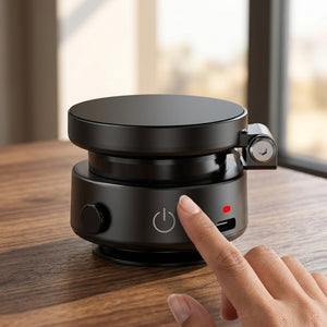 Black hot plate with power button on a wooden surface, hand pressing the button.