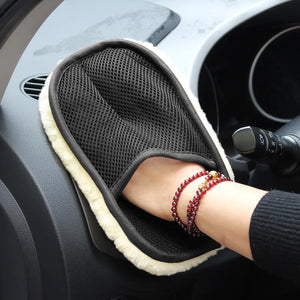 Hand wearing a black mesh glove with beige trim on a car dashboard.