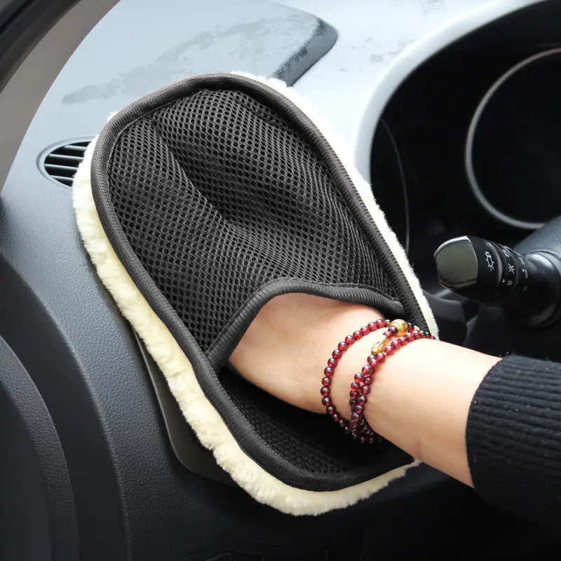 Hand wearing a black mesh glove with beige trim on a car dashboard.