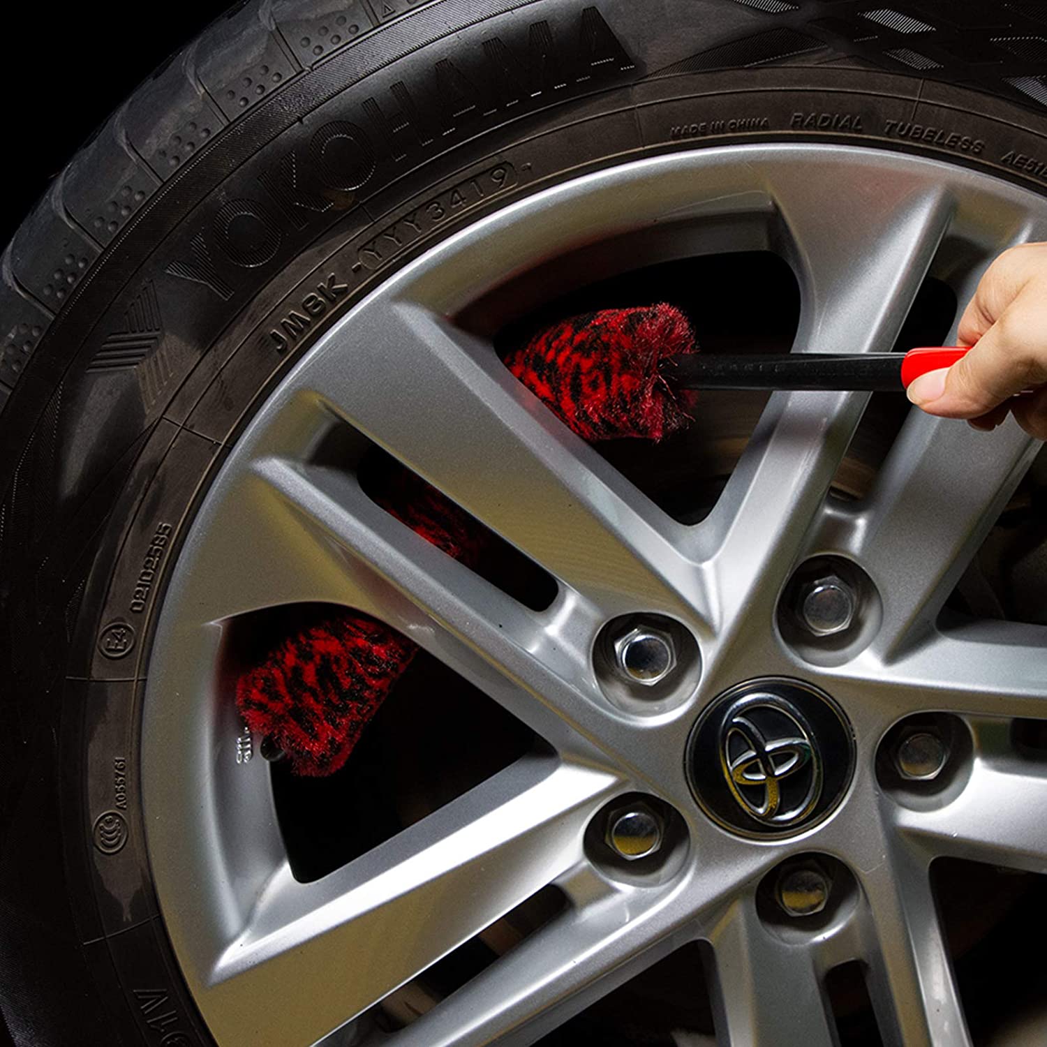 Person cleaning car wheel with a red brush